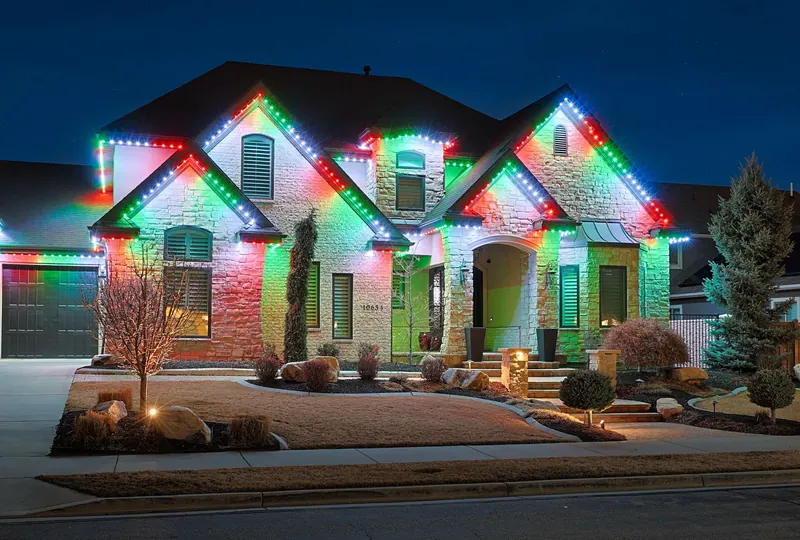 Stone home at night with red, green and white lights along every gable and eave